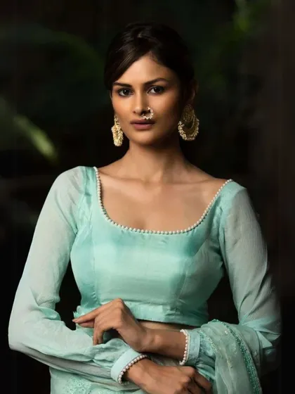 This model wears large, traditional gold-toned earrings that add a touch of ethnic glamour to her simple, elegant blouse.