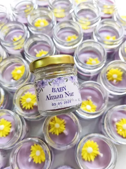 A close-up of the personalized mini jar candle for a baby announcement, featuring a custom sticker and a delicate flower topper.
