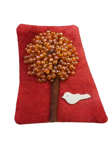 A handcrafted fabric patch featuring a tree made of amber-colored beads on a red jute base. This artistic pin adds a rustic and unique touch to bags, jackets, or scarves.