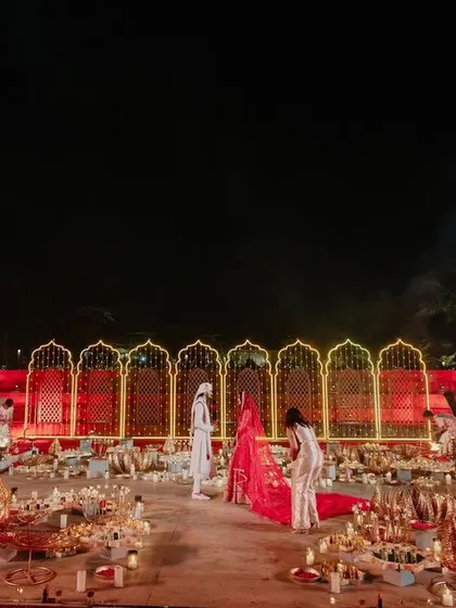 The epic Varmala ceremony unfolds in a grand amphitheater setting, with the couple framed by a glowing arch and surrounded by guests and candlelight.