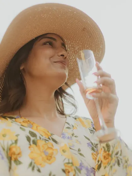 A portrait of the bride-to-be enjoying a glass of champagne during their picnic, looking radiant in her sun hat.