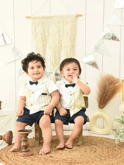Double the fun! These adorable twins are perfectly coordinated for their boho-themed photoshoot, sitting together on a rustic bench.