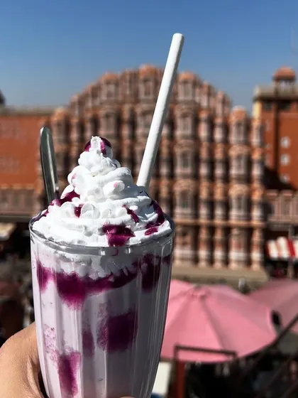A colorful blueberry milkshake with the Hawa Mahal softly blurred in the background. This composition keeps the focus on the refreshing drink while still giving a strong sense of place.