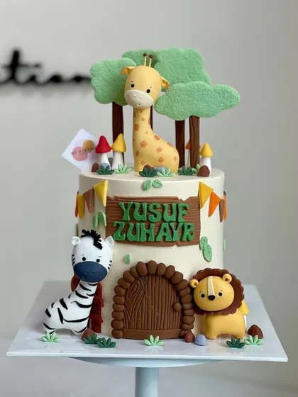 A sweet and simple jungle-themed cake for Yusuf Zuhayr. This design features a friendly lion, zebra, and giraffe around a little fondant door, perfect for a child's celebration.