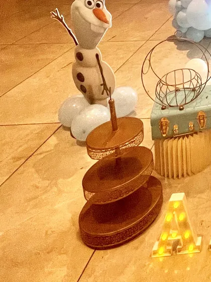 Themed props are key to an immersive party. Here you can see an Olaf cutout, a tiered serving stand, and a light-up marquee letter 'A' from a Frozen birthday party.