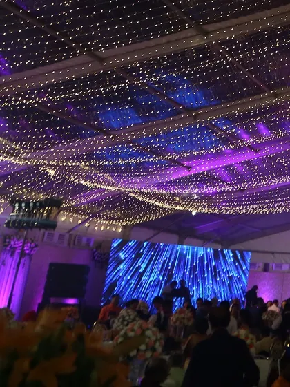 A ceiling of fairy lights creates a starry night effect inside a large tent. The purple and blue lighting on the stage and LED screen adds to the vibrant, celebratory atmosphere of a sangeet or reception.