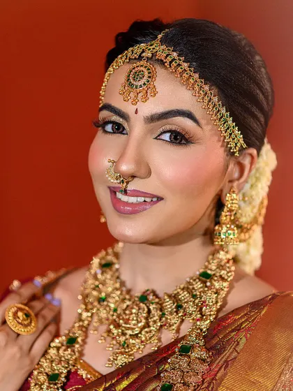 A close-up portrait capturing the bride's joyful expression. The warm lighting perfectly complements her golden jewellery and the rich tones of her saree.
