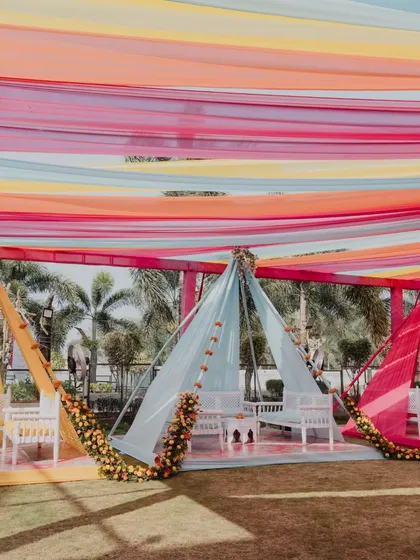 Colorful tented seating arrangements for an outdoor Haldi. We use vibrant drapes to create beautiful, shaded areas for guests to relax and enjoy the festivities.