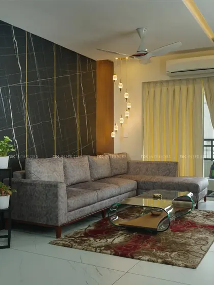 A luxurious living room with a dark marble accent wall featuring gold inlay. The plush grey sectional sofa and spiral hanging light fixture create a modern and glamorous feel.