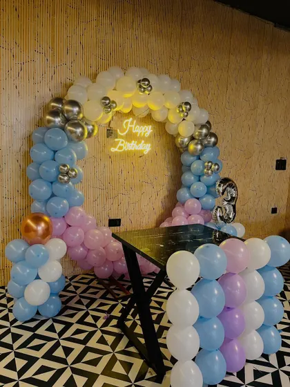 A pastel-themed 3rd birthday decoration with a balloon arch in light blue, pink, and white, accented with silver chrome balloons.