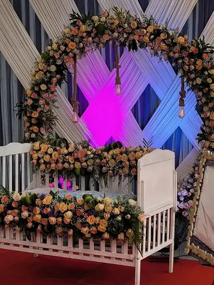 A close-up view of a white cradle lavishly decorated with peach and pink roses for a beautiful naming ceremony.
