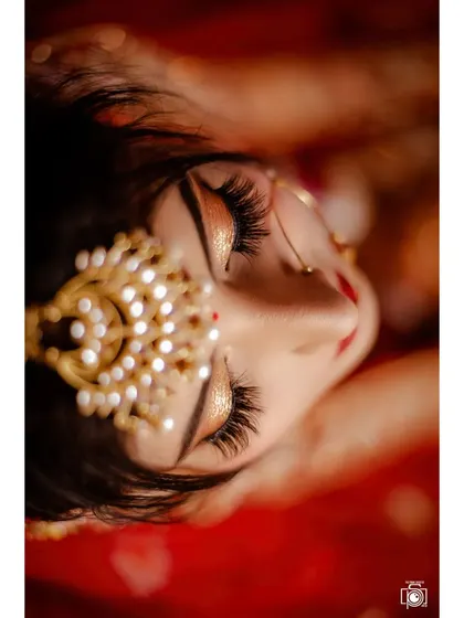 A creative top-down angle focusing on the bride's stunning eye makeup and pearl matha patti. This artistic bridal portrait captures the quiet, precious moments before the main ceremony.