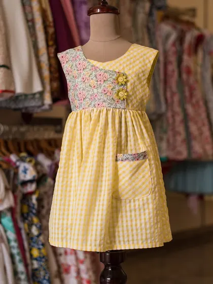 A cheerful yellow gingham dress with a floral print accent on the bodice. The single pocket with matching floral trim is a cute and quirky detail.