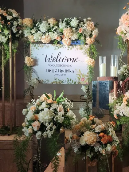 A chic welcome sign for a wedding, surrounded by lush arrangements of white and peach flowers.