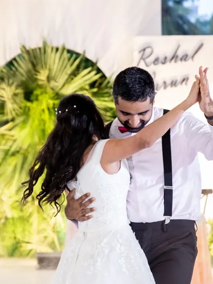 The couple shares a dance at their reception. The simple white arch backdrop with palm accents is perfect for a relaxed and intimate celebration.