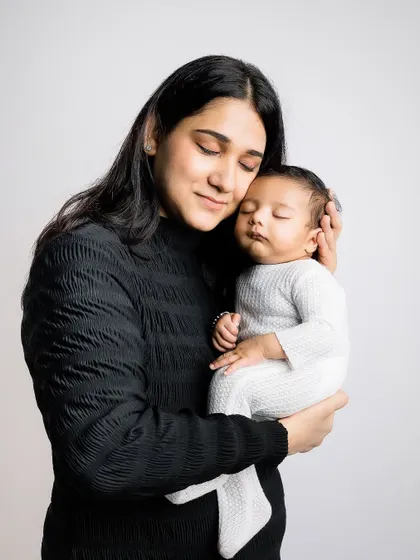 A mother in a classic black sweater holds her sleeping baby, creating a simple and elegant portrait.