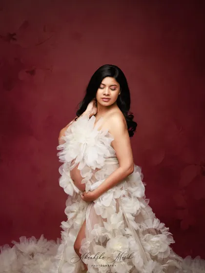 A quiet, introspective pose in the stunning white floral gown, highlighting its delicate texture and the mother's gentle connection with her bump.