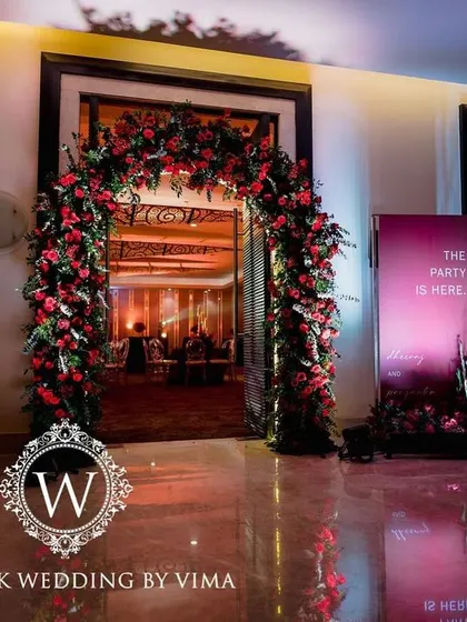 A bold and luxurious reception with a red and black color scheme. The decor includes rich red roses, modern crystal candelabras, and a stylish bar with a neon arch backdrop.