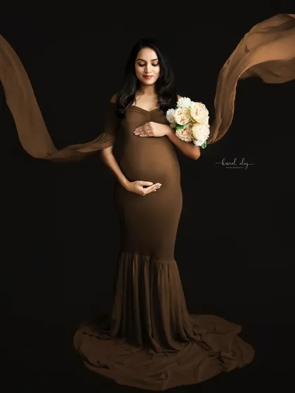 A fine-art maternity portrait featuring a flowing brown gown against a dark studio backdrop. The use of fabric in motion adds a dramatic and elegant effect to this solo pregnancy photo.