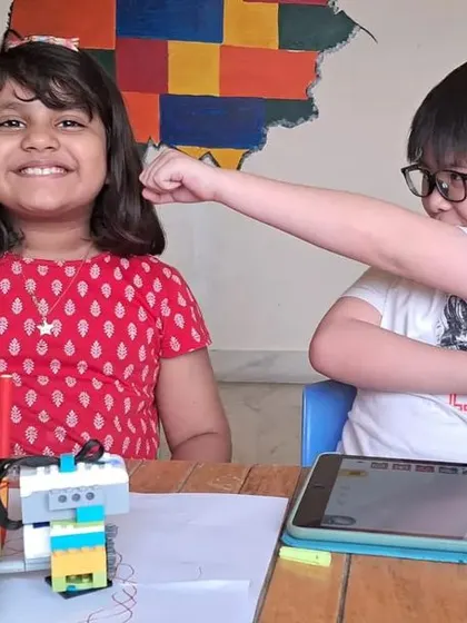 Two students having fun while learning, with one playfully interacting with the other's robotic creation.