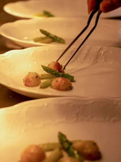 A warm, golden-lit shot of a chef plating with tweezers.