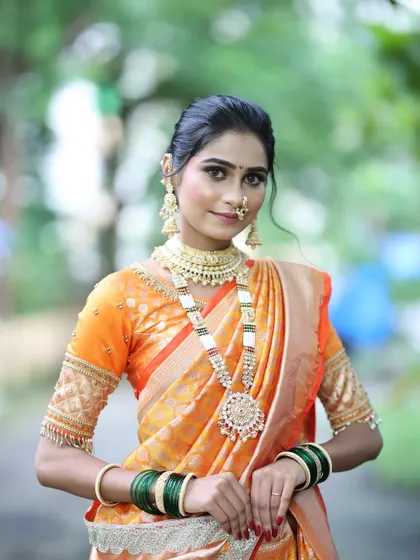 A full-length portrait of a bride in a stunning orange saree. The makeup is kept fresh and radiant to complement the bright color of her outfit.