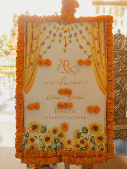This custom welcome sign for a Haldi ceremony features a sunflower and marigold theme, with a frame made of fresh marigolds to greet guests with traditional warmth.