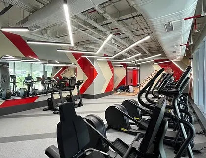 The cardio section is defined by bold red and white graphics on the walls, which visually guide users through the space. The open layout and large windows provide ample natural light for a more pleasant workout.