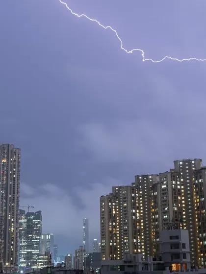 A horizontal lightning bolt flashes across the sky above a cluster of buildings in Mumbai.