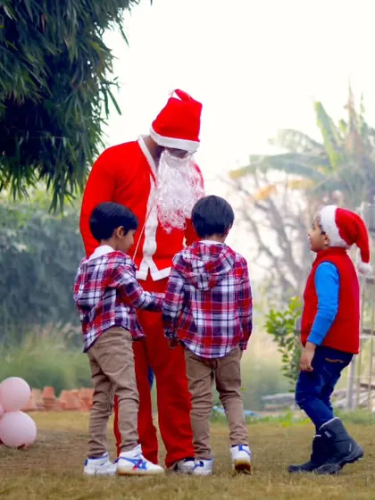 A heartwarming photo of Santa Claus interacting with three young boys in matching plaid shirts.