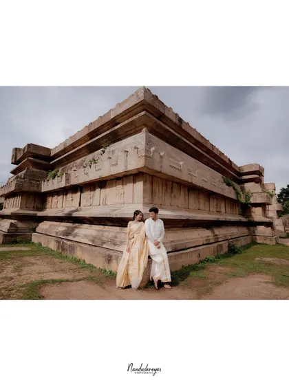 A wide shot of a couple sitting together against a massive, pyramid-like stone temple structure, showcasing the scale and grandeur of a heritage location shoot.