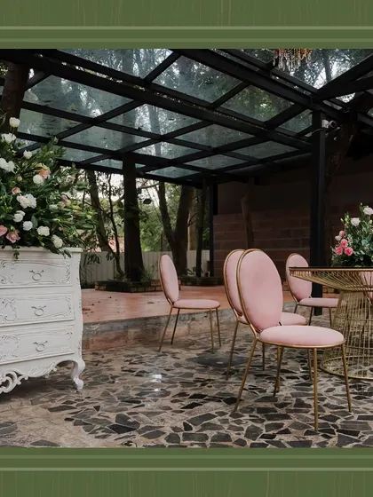 Chic pink chairs and a gold table sit under the glass-roofed structure at the brunch event. This luxurious seating area allowed guests to enjoy the surrounding nature in comfort and style.