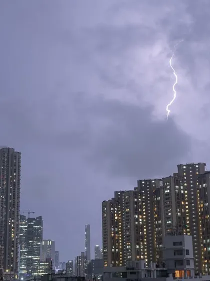 A single, bright lightning strike is captured in the cloudy night sky over Mumbai.