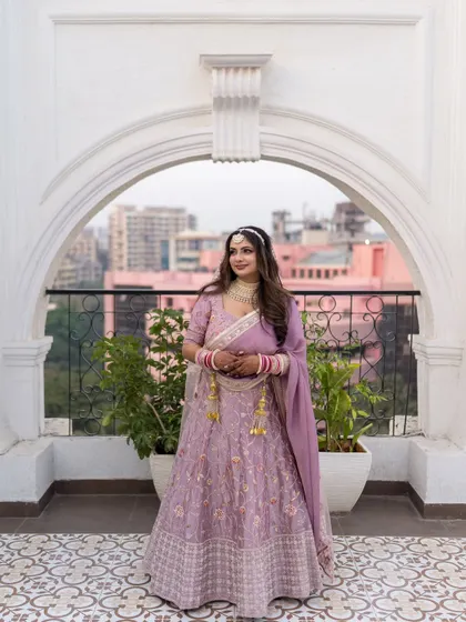 A stunning architectural portrait of the bride, Nitika, framed by a white archway that complements her elegant lehenga.