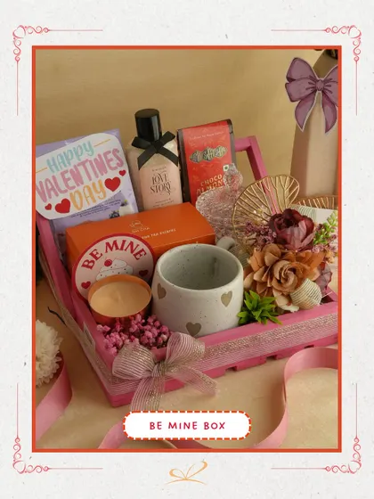 The 'Be Mine Box' is a classic romantic gesture. This pink wooden tray is filled with a heart-themed mug, a scented candle, skincare products, and a 'Be Mine' tag, making your intentions clear.
