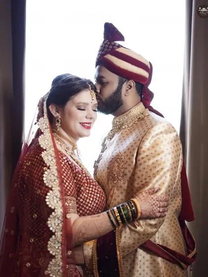 A loving embrace between a bride and groom, captured in soft, natural light. The groom's kiss on the bride's forehead conveys a sense of tenderness and protection.