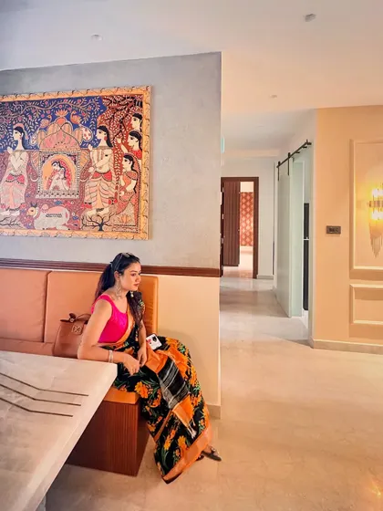 A shot of me sitting in a dining nook with a large Pattachitra painting on the wall, demonstrating how art is integrated into daily life.