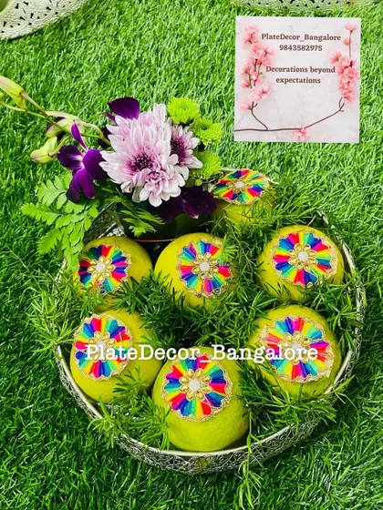 Sweet limes decorated with multi-colored threadwork medallions, nestled in a bed of green leaves and topped with fresh flowers.