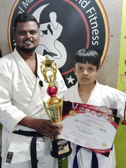 This young student proudly holds his first and third-place trophies, a testament to his versatile skills in karate.