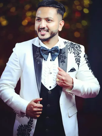 A custom-designed white tuxedo created for a client's special event. This piece features intricate black embroidery on the shoulders and lapels, paired with a classic waistcoat and bow tie, all tailored for a guaranteed perfect fit.