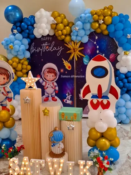 An outer space themed birthday party with a galaxy backdrop and astronaut cutouts. The setup includes wooden-style plinths, star props, and the child's name in marquee letters.
