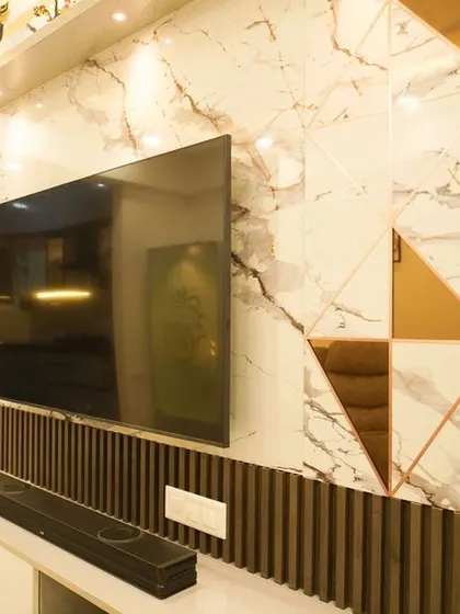 A close-up of the TV wall, showcasing the combination of a large-format marble-finish panel, dark wood fluting, and geometric bronze mirror accents for a luxurious and contemporary feel.