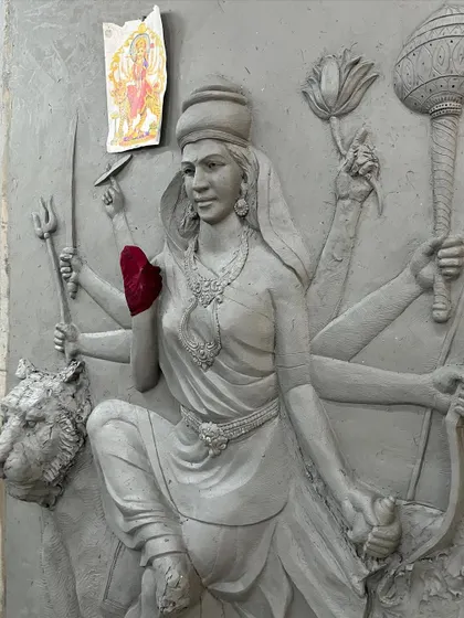 The clay sculpture of Maa Durga from a different perspective, showcasing the complexity of her multiple arms and the weapons she holds.