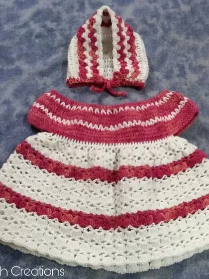 A beautiful hand-crocheted baby dress and matching bonnet set, featuring a striped pattern in shades of pink and white.