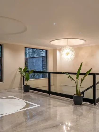 The upper lobby area of a project, featuring a minimalist design with marble flooring, inlay details, and a modern chandelier. The space feels open and luxurious, with a glass railing overlooking the floor below.