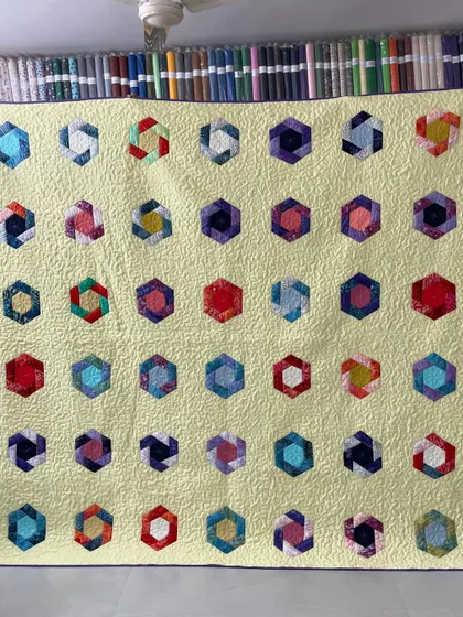 A beautiful quilt featuring colorful, scrappy hexagons arranged on a pale yellow background.