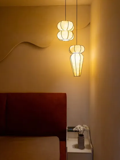 The interplay of light and shadow from the unique pendant lights against the textured wall in the 'Sukoon' bedroom.