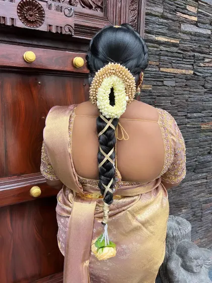 A traditional braid with a gold ribbon criss-cross pattern, a jasmine gajra with a central opening, and a floral tassel.