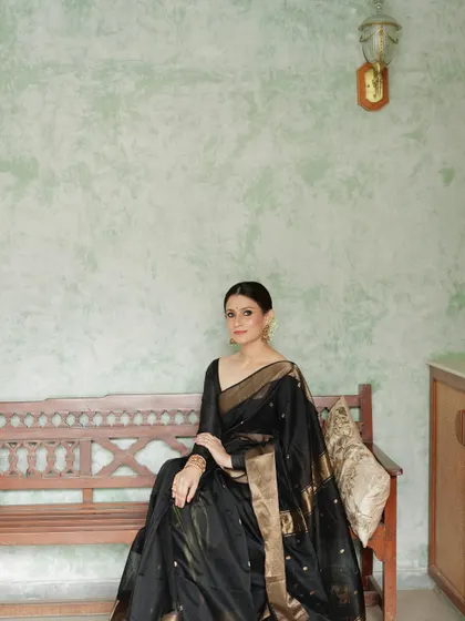 A seated portrait in the black and gold saree, conveying an aura of sophisticated grace.