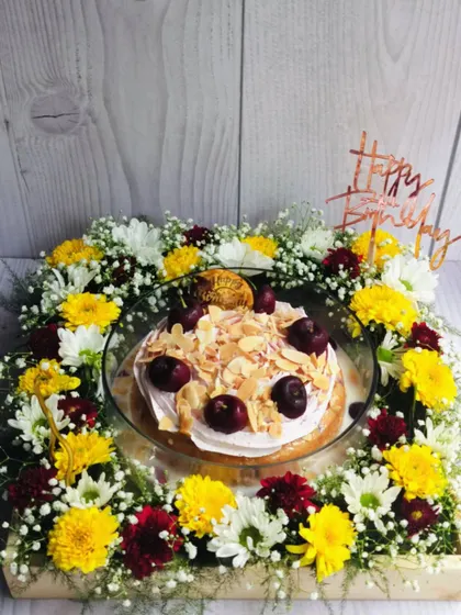 The full presentation of the Cherry Almond Tres Leches Floral Hamper, showing the cake in its glass dish, nestled within a wooden crate filled with a vibrant floral arrangement.